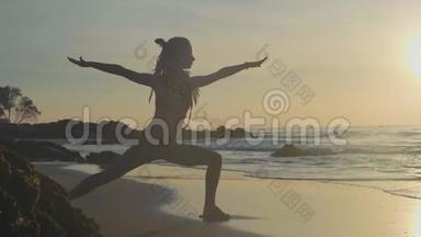 日落时剪影瑜伽练习。 勇女在沙滩上做瑜伽运动